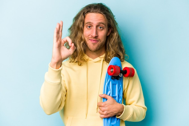 Young skater caucasian man isolated on blue background cheerful and confident showing ok gesture