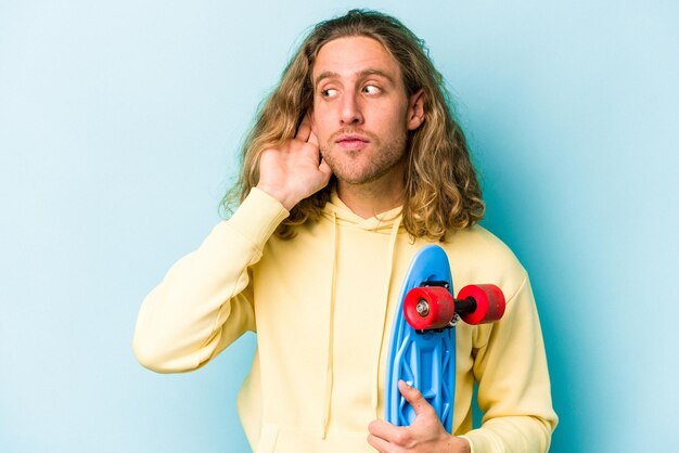 Young skater caucasian man isolated on blue background trying to listening a gossip