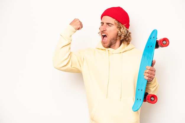 Young skater caucasian man isolated on white background raising fist after a victory, winner concept.