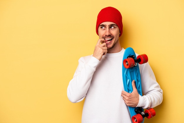 Young skater caucasian man isolated on yellow background relaxed thinking about something looking at a copy space.