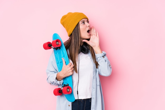 Young skater woman holding a skate shouting and holding palm near opened mouth.