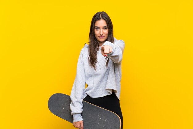 격리 된 노란색 벽을 통해 젊은 스케이팅 여자는 자신감을 표현 손가락 당신을 가리키는