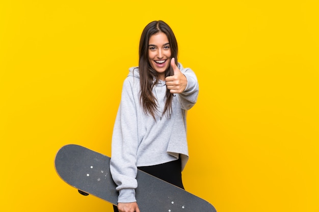 Young skater woman over isolated yellow wall with thumbs up because something good has happened