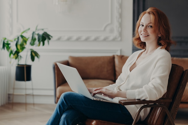 Young skilled woman writer types or keyboards text for new book on laptop computer, feels comfort in cozy room, searches information in internet, works from home. Student busy with coursework