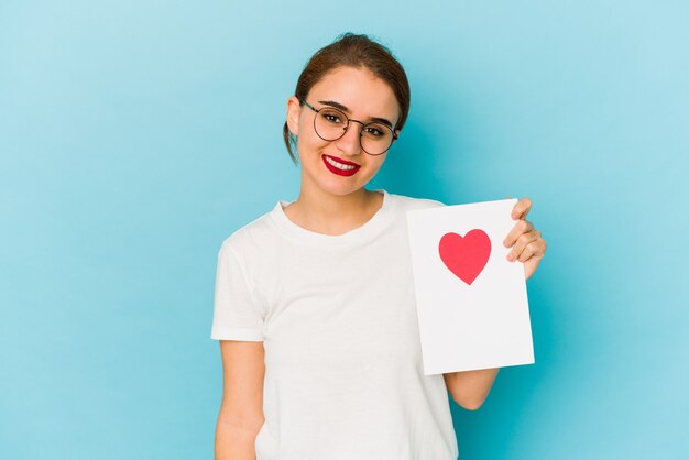 Young skinny arab girl holding a valentines day card happy, smiling and cheerful.