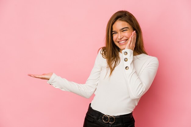 Young skinny caucasian teenager girl holds copy space on a palm, keep hand over cheek. Amazed and delighted.