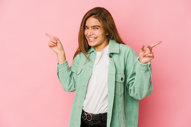 Young skinny caucasian teenager girl pointing to different copy spaces, choosing one of them, showing with finger.