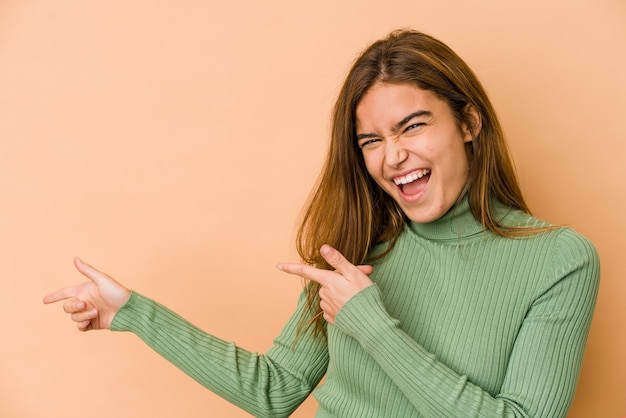 Young skinny caucasian teenager girl pointing with forefingers to a copy space, expressing excitement and desire