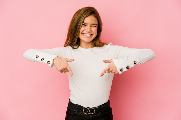 Young skinny caucasian teenager girl points down with fingers, positive feeling.