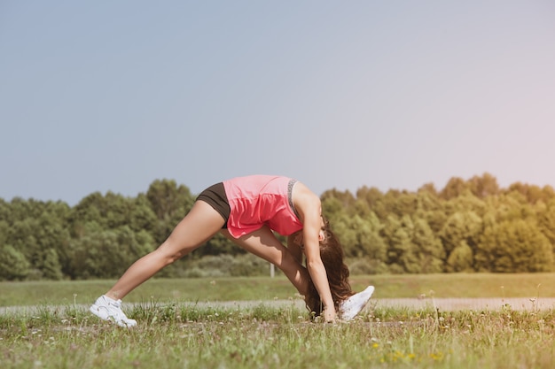 Young skinny girl doing exercise on the grass.