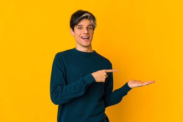 Young skinny hispanic man excited holding a copy space on palm