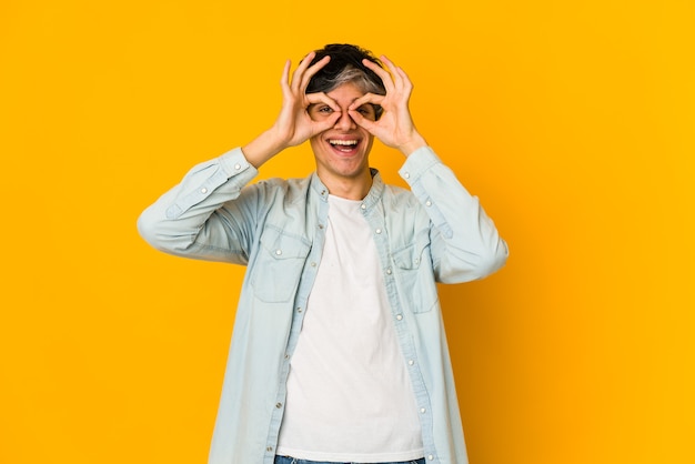 Young skinny hispanic man excited keeping ok gesture on eye.