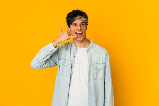 Young skinny hispanic man showing a mobile phone call gesture with fingers.