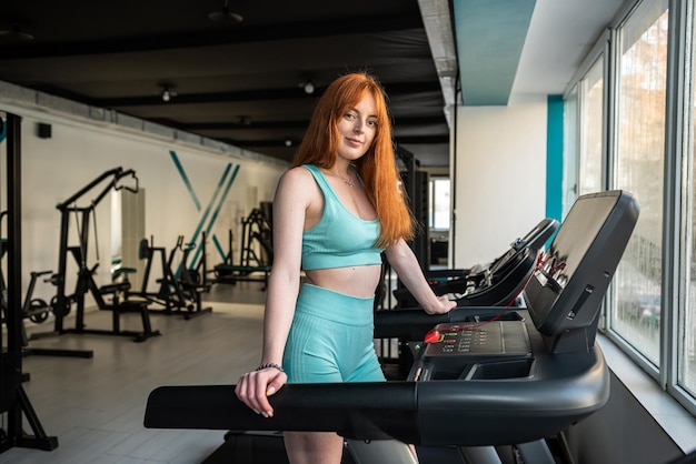 Young skinny sporty female athletic stand near treadmill trainers and rest after exercise at gym