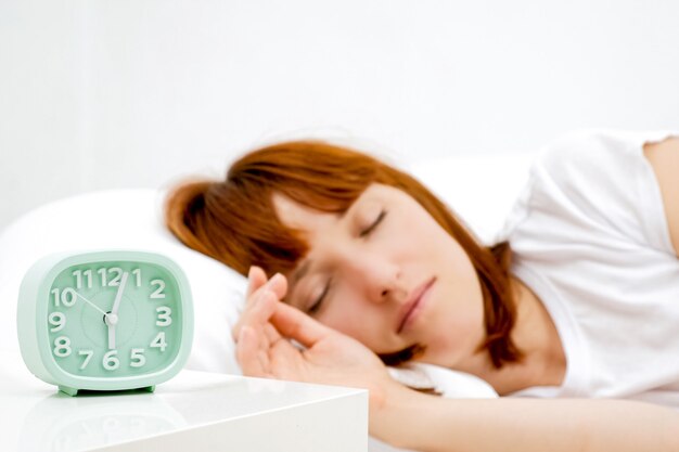 Young sleeping woman and alarm clock in bedroom at home.