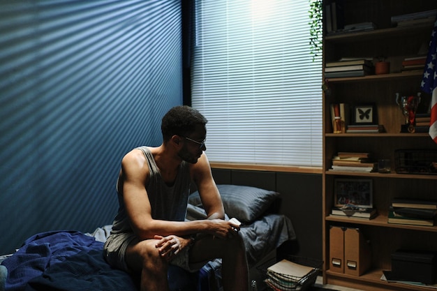 Young sleepless man in underwear and eyeglasses sitting on bed at midnight