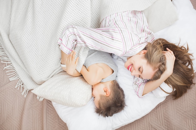 彼女の幼い息子と一緒にベッドで横になっている眠そうな若い母親。家族との日曜日の朝