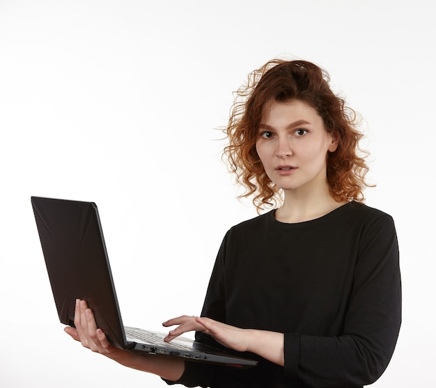 A young slender girl in black clothes works on a laptop. Figure isolated on a white background.