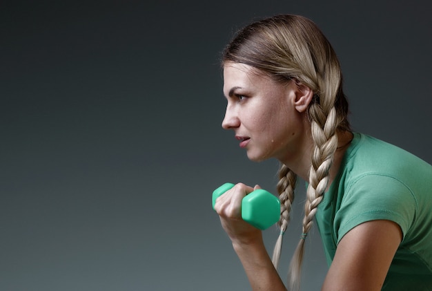 Young slender girl works with small dumbbells performing exercises. concept of a healthy lifestyle. gray background. studio light