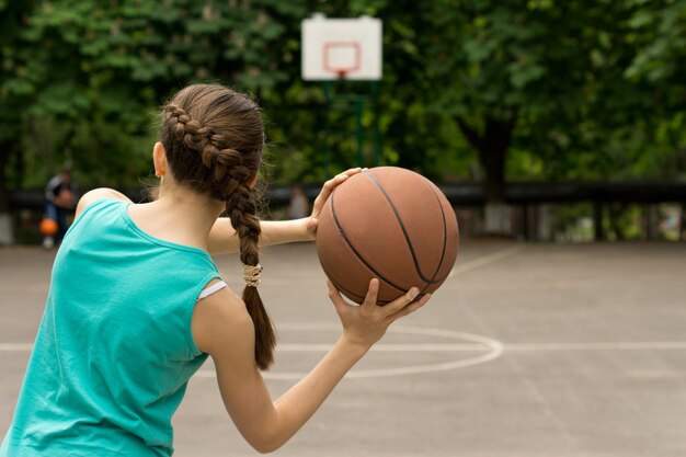 Foto giovane ragazza adolescente snella che gioca a basket lanciando la palla, vista da dietro