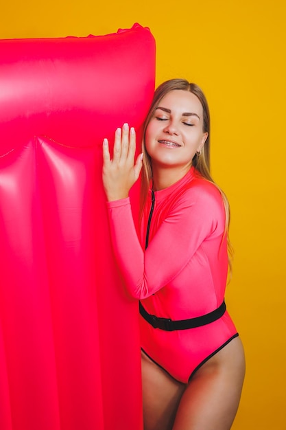 Young slender woman in a pink swimsuit on a yellow background Girl with an inflatable mattress for swimming in the pool Summer vacation