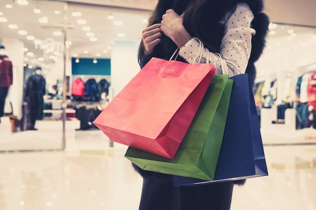 白いブラウスとファーのチョッキを着た若いほっそりした女性が買い物袋を持ち、モールで買い物をする