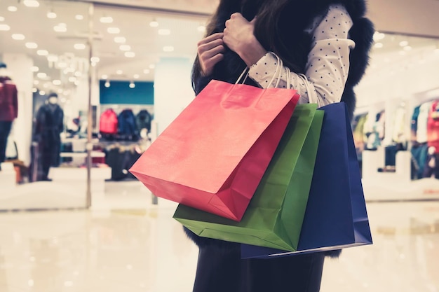 Young slender woman in white blouse and fur waistcoat holding shopping bags and doing shopping in mall cropped Faceless lady carrying heap of packages after purchasing in store Female expenses