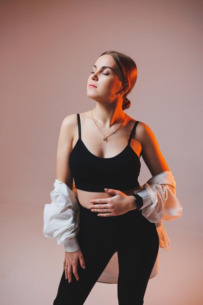 A young slender woman in a white shirt and black pants with makeup on her face poses on a plain background Stylish European woman in a black top