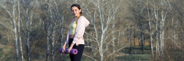 A young slim athletic girl in sportswear performs a set of exercises Fitness and healthy lifestyle against the background of green spring pasture hills