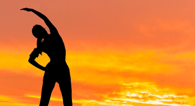 A young slim athletic girl in sportswear performs a set of exercises Fitness and healthy lifestylex9Silhouette at sunset