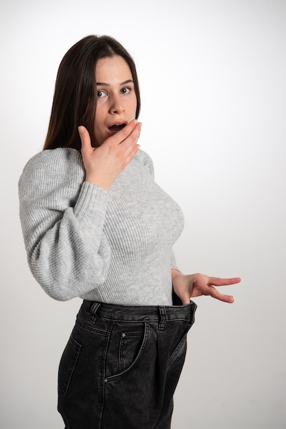 Young slim brunette girl in big jeans showing successful weight loss and yawning It was easy to reduce weight Diet concept Copy spacexDxA