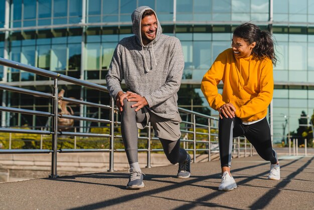 Young slim couple stretching together in sporty outfit outdoors with modern urban background