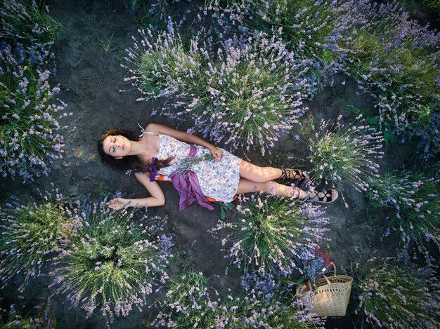 Young slim fair-skinned girl brunette beautiful lies in lavender field. Top view.