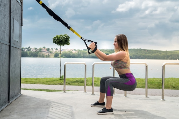 Foto giovane atleta femminile esile che si allena utilizzando trx in natura. uno stile di vita sano. rendi la tua macchina del corpo