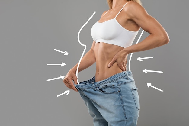 Foto giovane femmina esile tirando grandi jeans e mostrando il risultato della perdita di peso