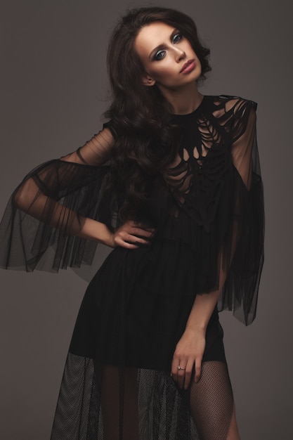 Young slim girl in black sexy fashionable dress. posing in the studio. long black hair