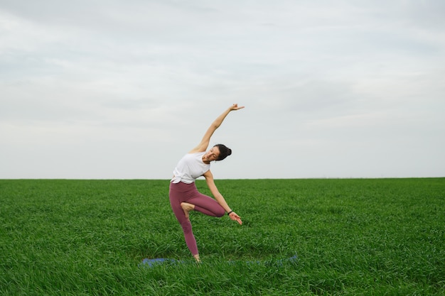 Молодая худенькая девушка занимается йогой на открытом воздухе в зеленом поле