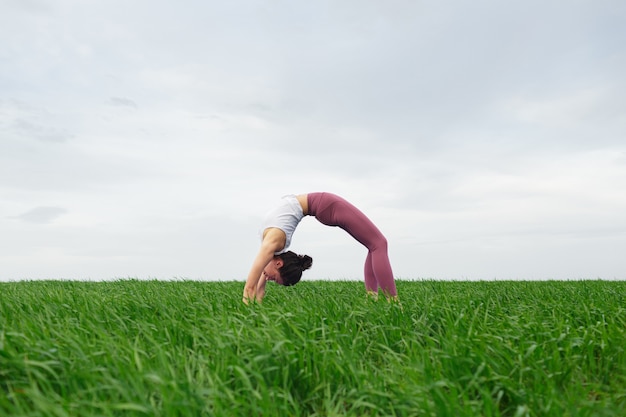 Foto giovane ragazza sottile che fa yoga all'aperto in un campo verde