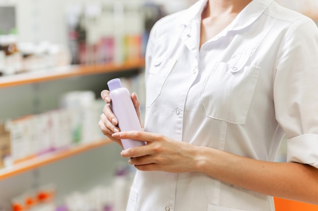 Una giovane ragazza snella, vestita con un camice bianco, tiene in mano uno spray in una nuova farmacia. .