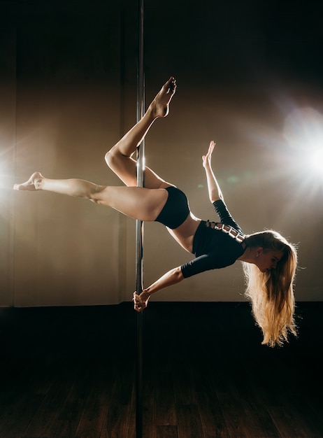 Young slim sexy woman pole dancing on dark background with lights