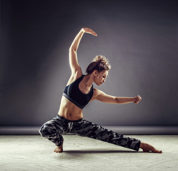 Молодая стройная женщина танцор в спортивной одежде прыгает высоко на фоне стены