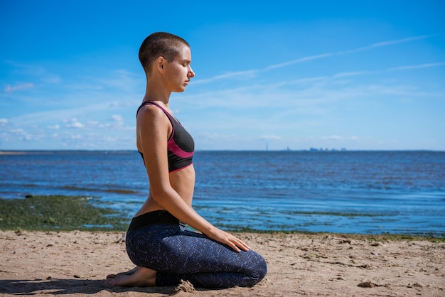 Young slim woman doing yoga outdoors on sandy shore bay on sunny day Unity