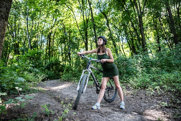 Young slim woman in green dress on bike standing on road and rest after trip