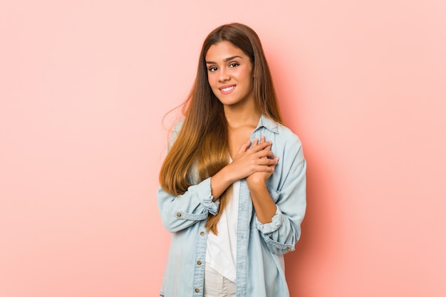 Young slim woman has friendly expression, pressing palm to chest