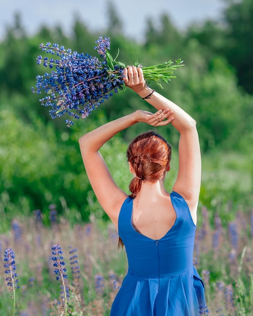 Фото Молодая стройная женщина в голубом платье с букетом голубых цветов вид сзади на девушку на летней природе