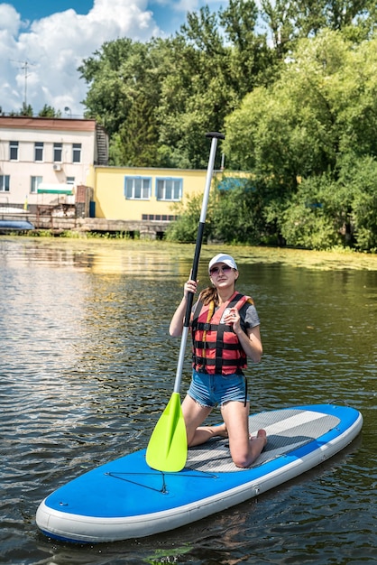 Young slim woman is riding a SUP board on the city lake enjoys a free summer hot day