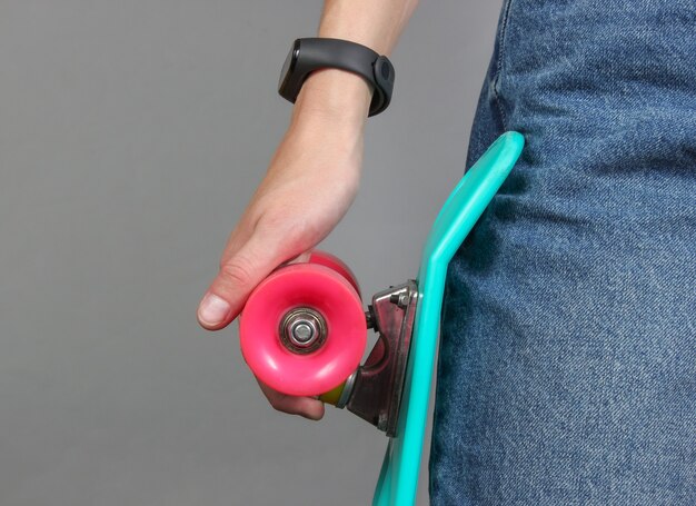 Young slim woman in jeans holds a plastic skate in her hands on a gray background. Youth hipster fashion. Crop photo. Copy space