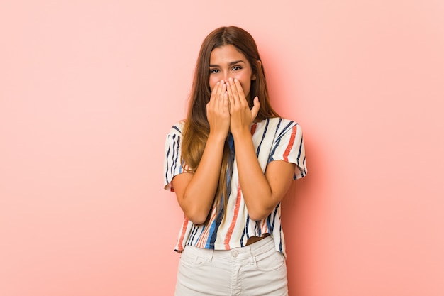 Young slim woman laughing about something, covering mouth with hands.