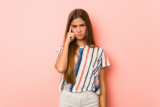 Young slim woman pointing temple with finger, thinking, focused on a task.