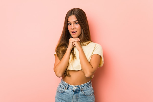 Young slim woman praying for luck, amazed and opening mouth looking to front.